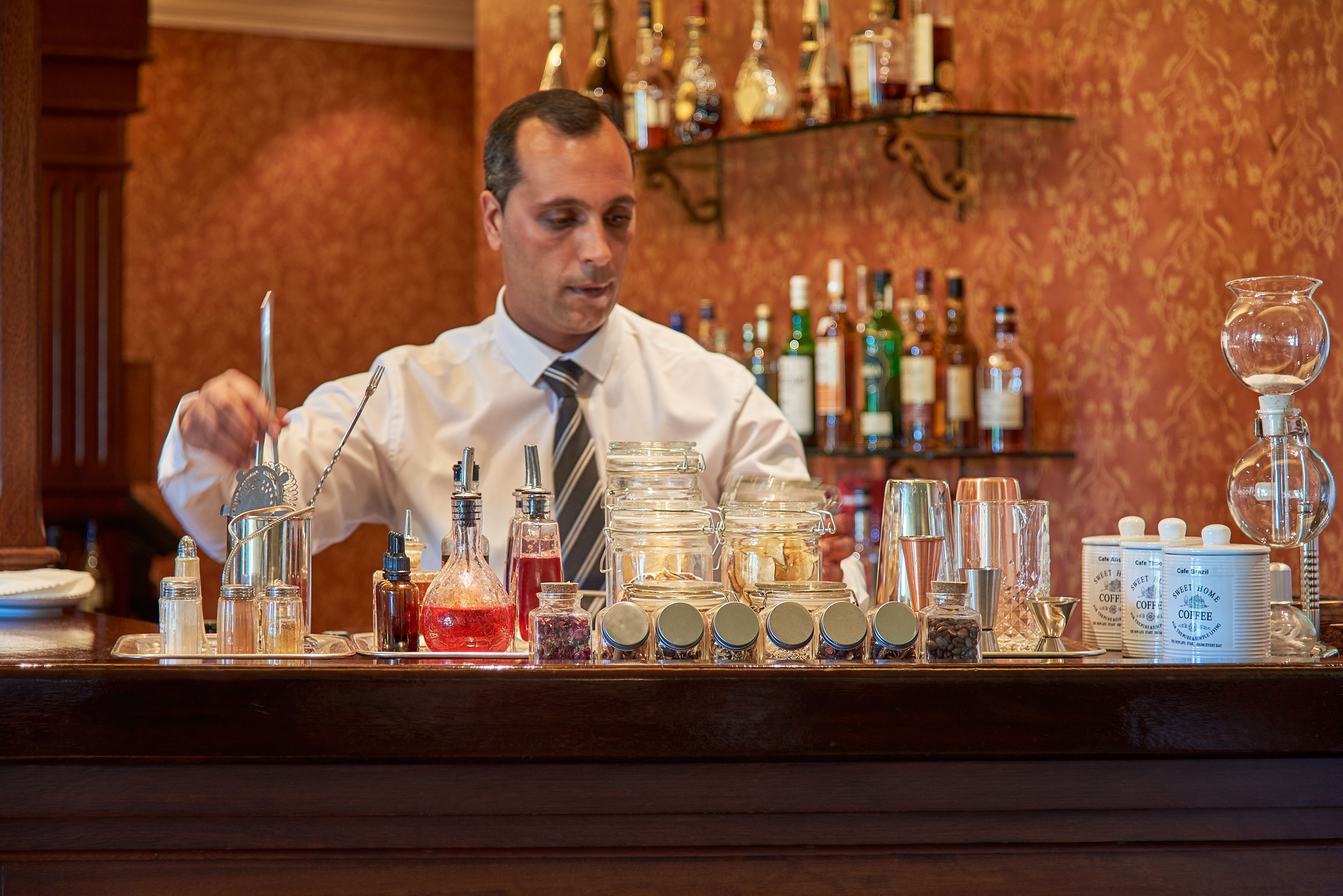 A bar area with a variety of glassware, bottles, and jars on the counter.