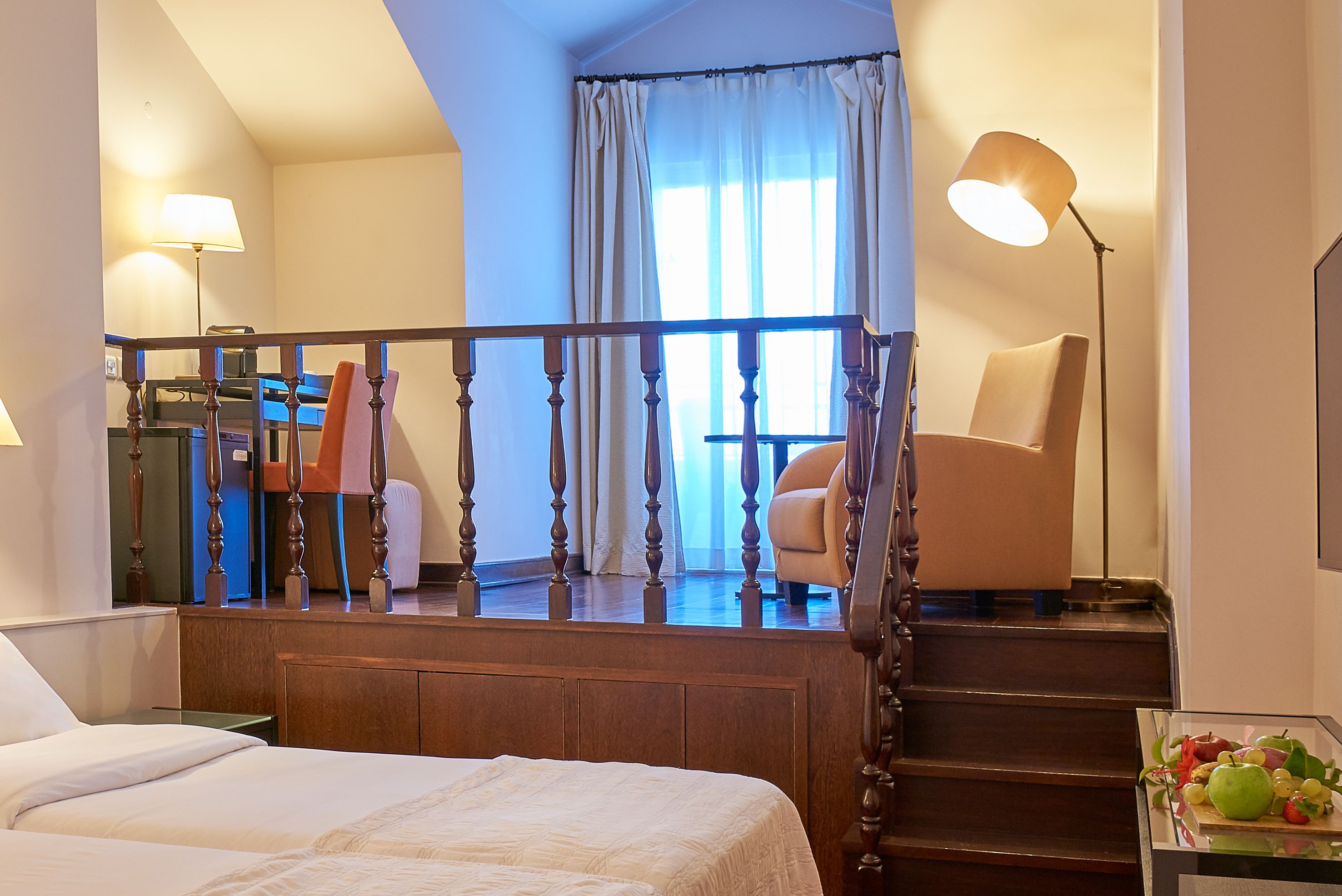 Ein Hotelzimmer mit Bett, Schreibtisch, Stuhl, einer Treppe und Blick ins Freie.