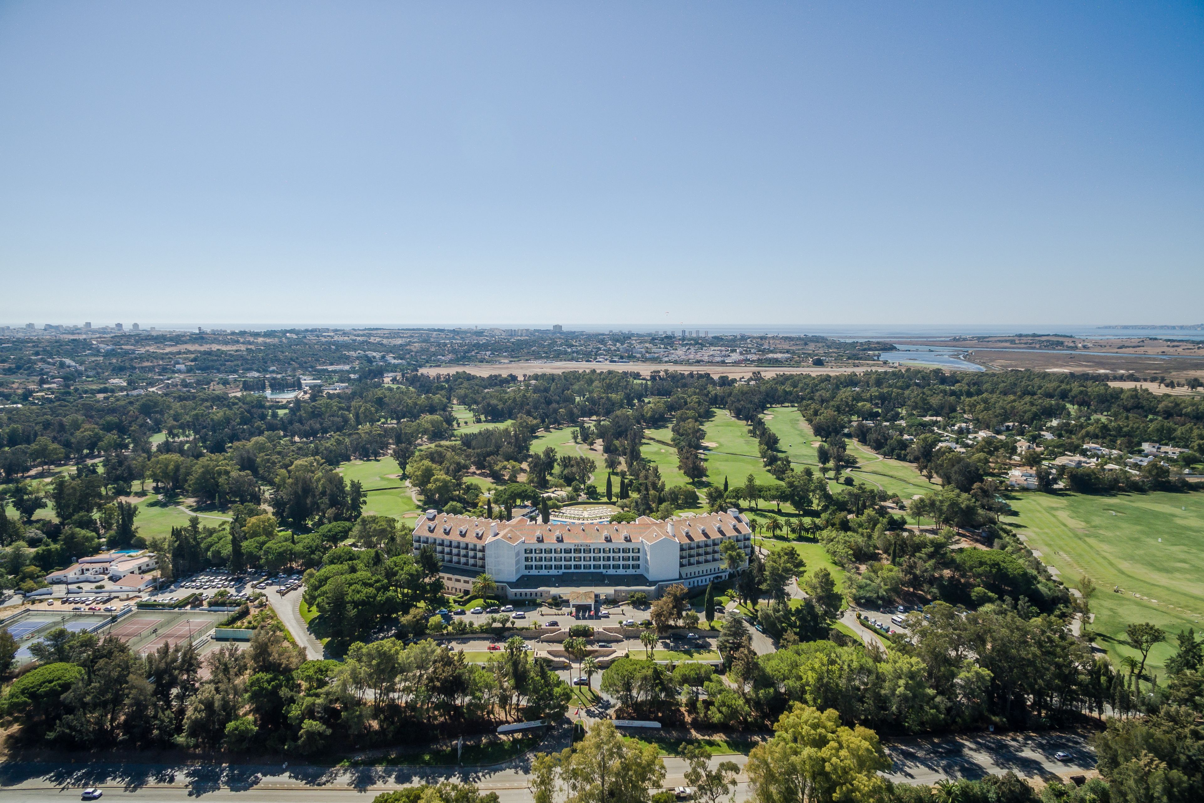 Vista aérea de un hotel grande y circular con varios pisos, rodeado de vegetación exuberante y un campo de golf.