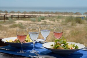 Una mesa dispuesta con dos ensaladas y tres vasos de agua, con vistas a la playa.
