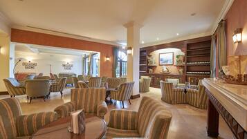 A spacious lobby with striped armchairs, a wooden coffee table, and a wine rack.