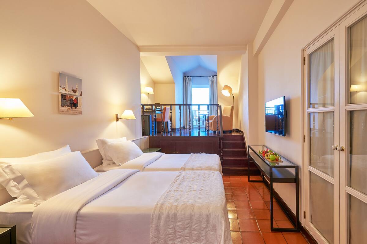 Une chambre d’hôtel avec deux lits, une télévision, un bureau avec une lampe et un escalier menant à un balcon.