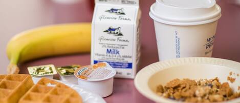 A table with a banana, a carton of milk, a coffee cup, a waffle, and a bowl of cereal.