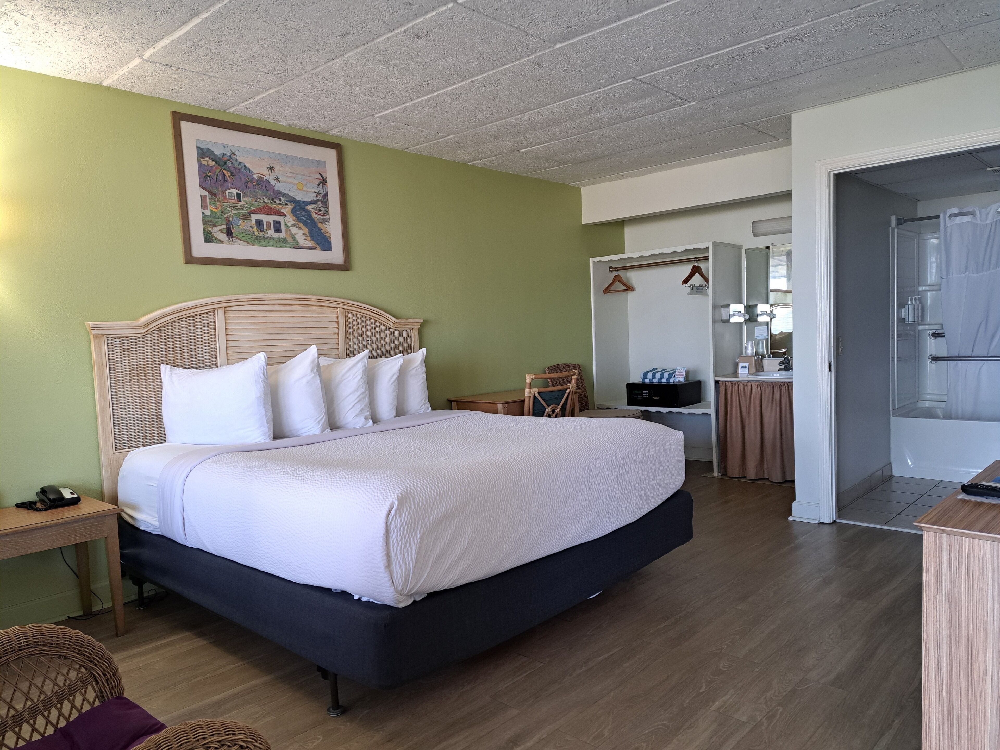 Ein Schlafzimmer mit einem großen Bett, einem Nachttisch, einem Sessel und einem durchgehenden Türspalt sichtbaren Badezimmer.