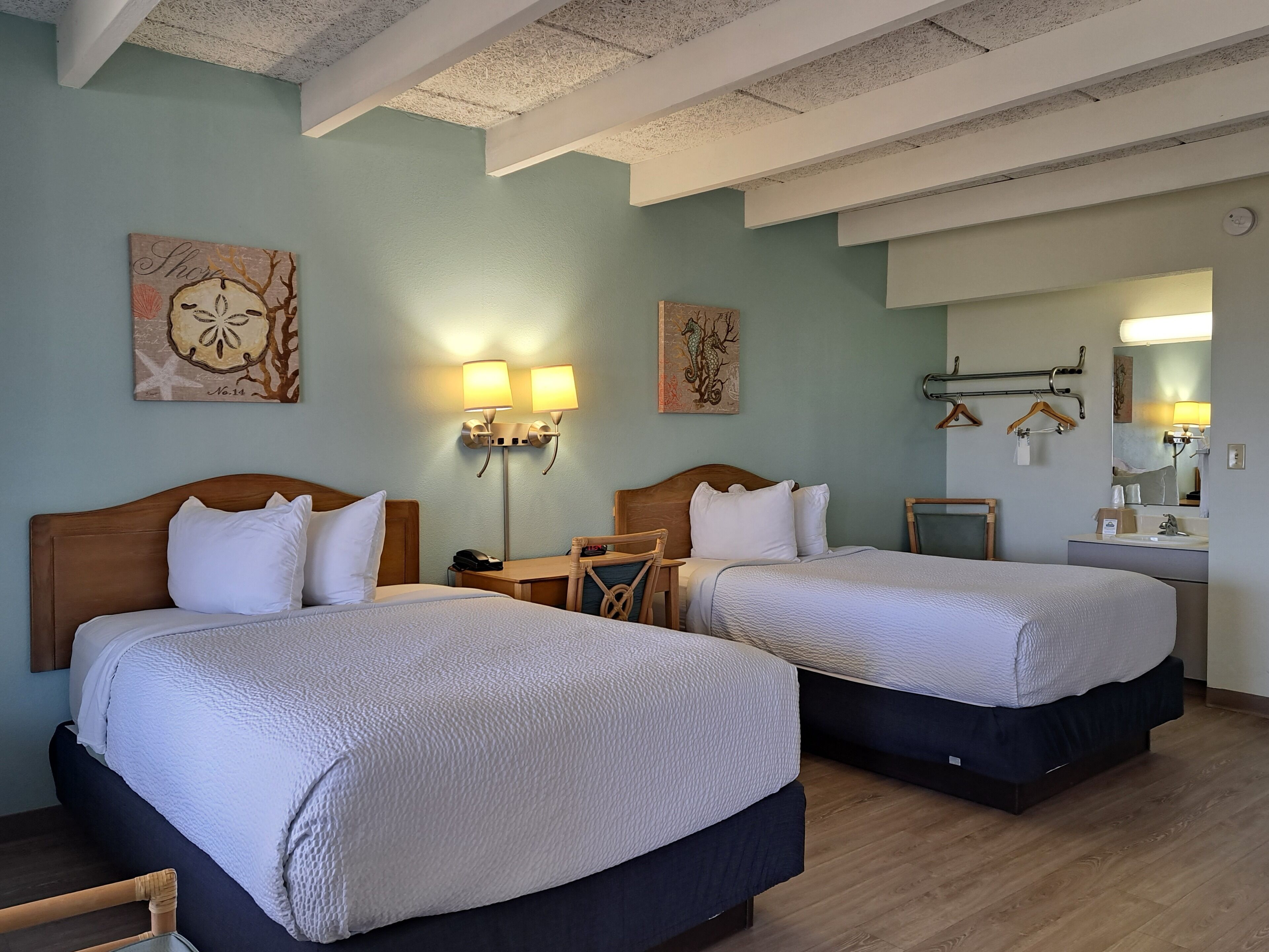 Habitació d'hotel amb dos llits, una tauleta de nit, una cadira, un escriptori, un mirall i decoració mural.
