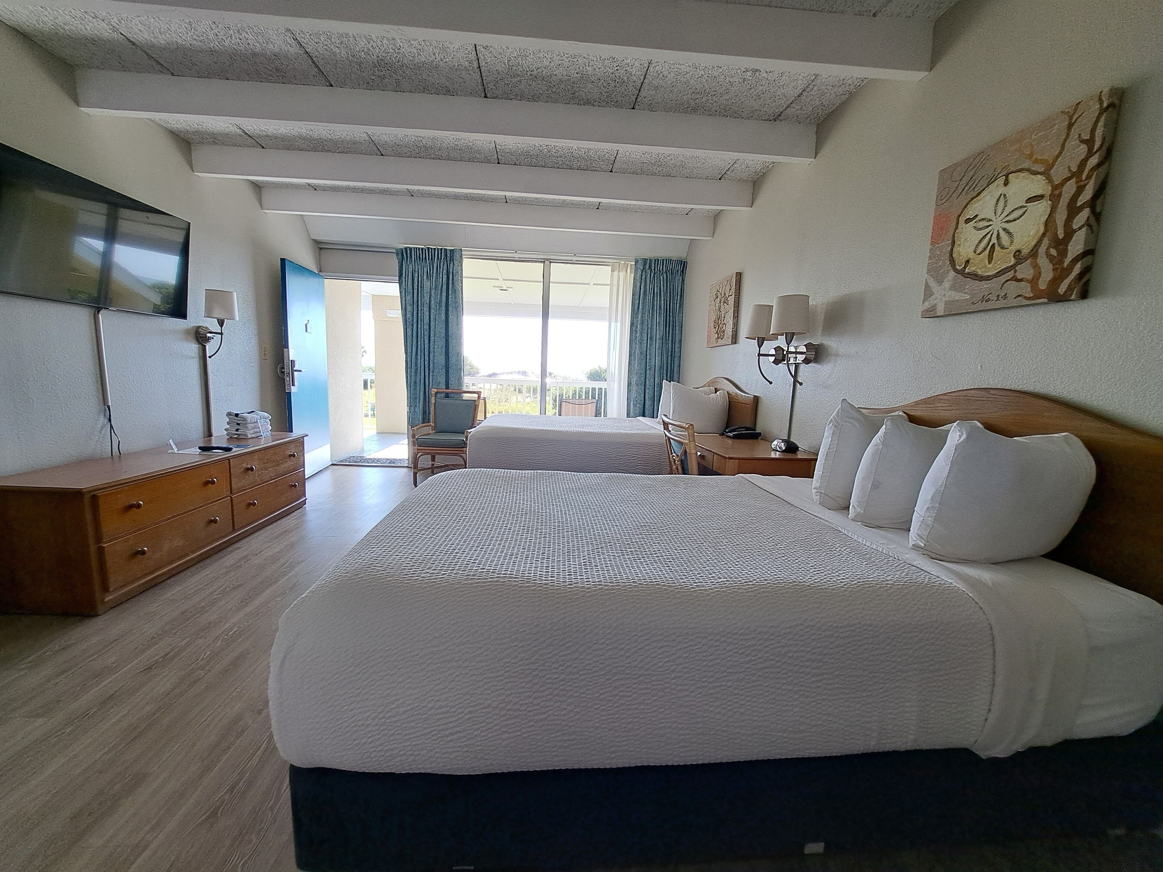 A hotel room with a large bed, a desk, a chair, a dresser, and a TV.