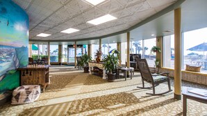 A spacious lobby with a large chess table, comfortable seating, potted plants, and large windows offering views of palm trees and a beach. - Days Inn & Suites by Wyndham Jekyll Island (Jekyll Island)