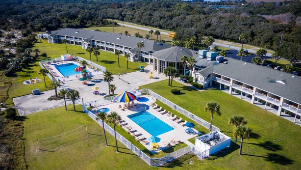An aerial view of a resort with two swimming pools, sun loungers, umbrellas, and a beach volleyball court. - Days Inn & Suites by Wyndham Jekyll Island (Jekyll Island)