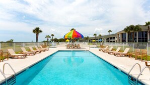 A swimming pool with lounge chairs and a colorful umbrella. - Days Inn & Suites by Wyndham Jekyll Island (Jekyll Island)