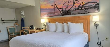 Een hotelkamer met een groot bed, een houten hoofdbord, een nachtkastje met een lamp, een stoel en een schilderij van een zonsondergang.