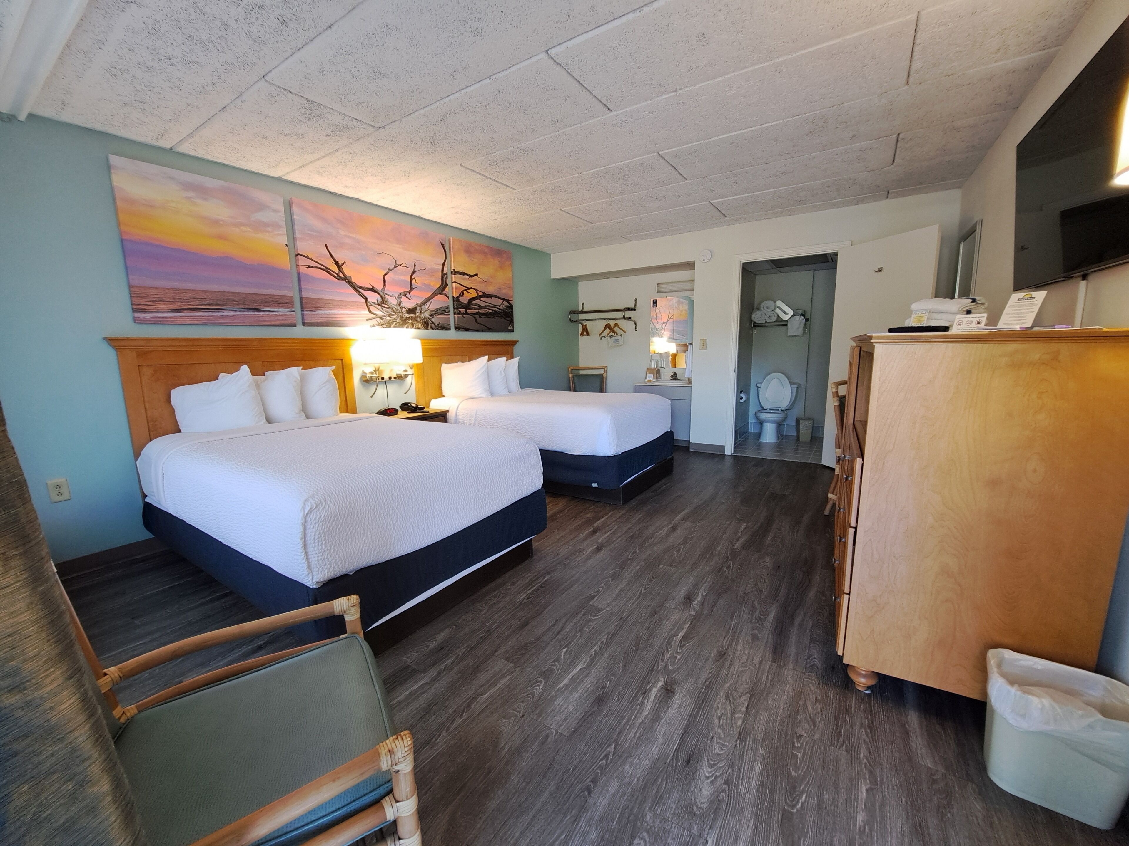 Habitación de hotel con dos camas, un aparador de madera, una silla y un cuadro en la pared.