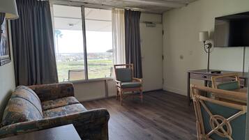 A room with a sofa, a chair, a desk, a television, and a window with curtains.