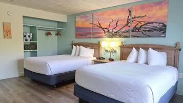 A hotel room with two beds, a nightstand with a lamp, a wall clock, and a painting of a sunset.