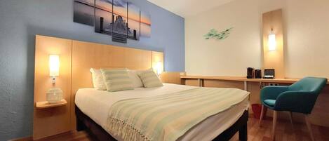 A hotel room with a bed, bedside lamps, a desk, a chair, and a wall art piece.