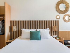 Een hotelkamer met een bed, een nachtkastje met lamp, een spiegel aan de muur en een houten hoofdbord.
