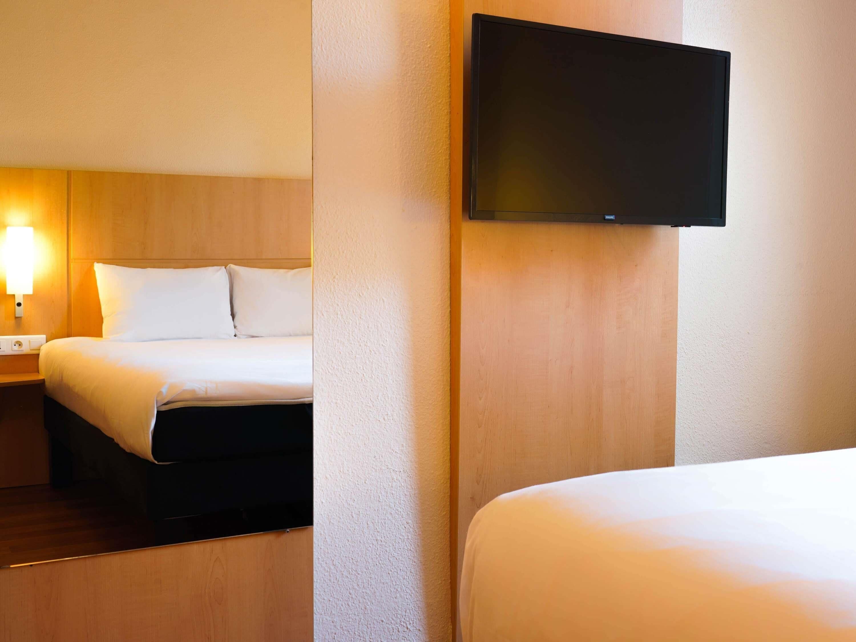 A hotel room with a bed, a nightstand, a lamp, and a flat-screen TV mounted on the wall.