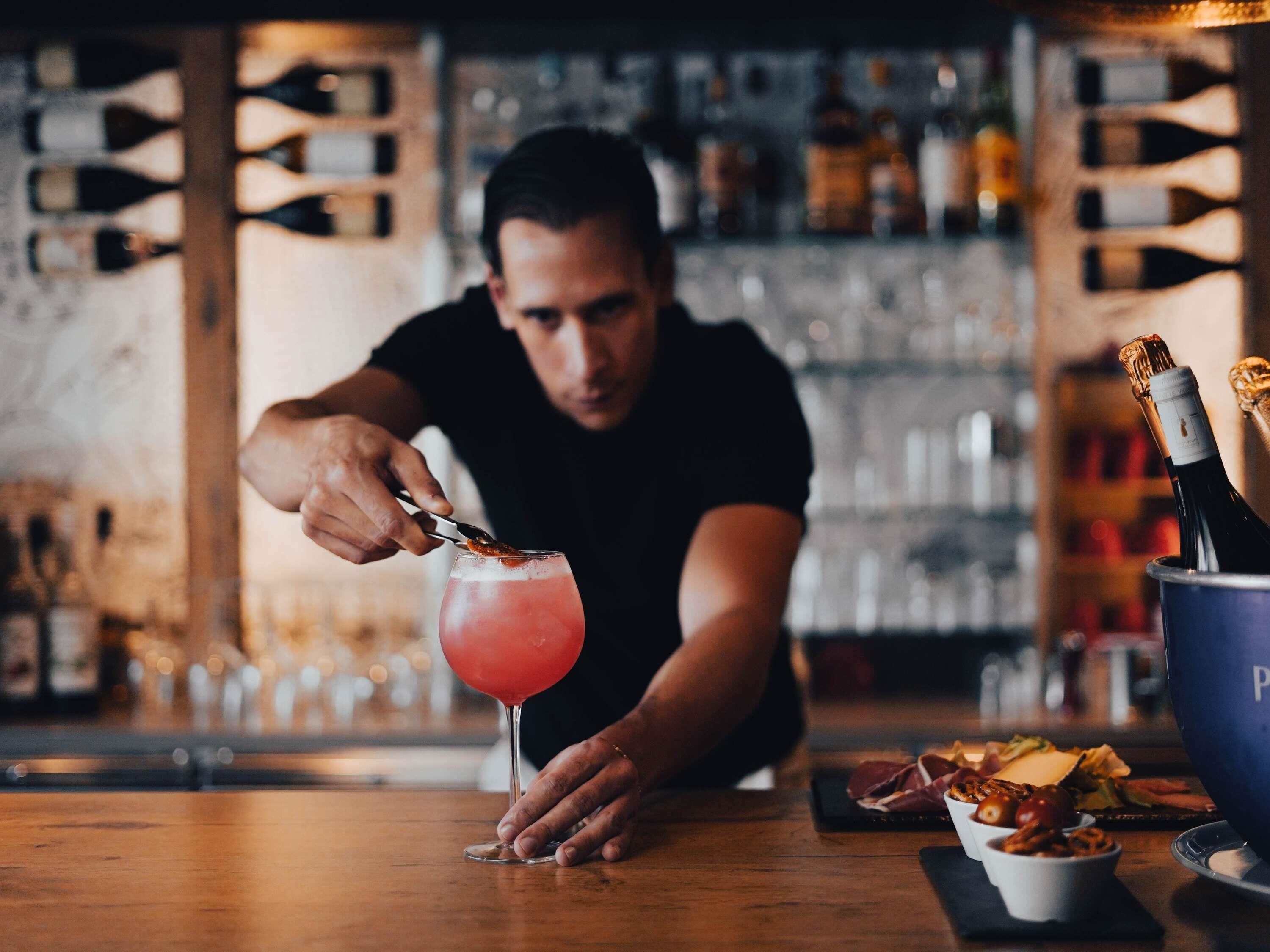 A bartender preparing a cocktail with a bottle of champagne in the background.