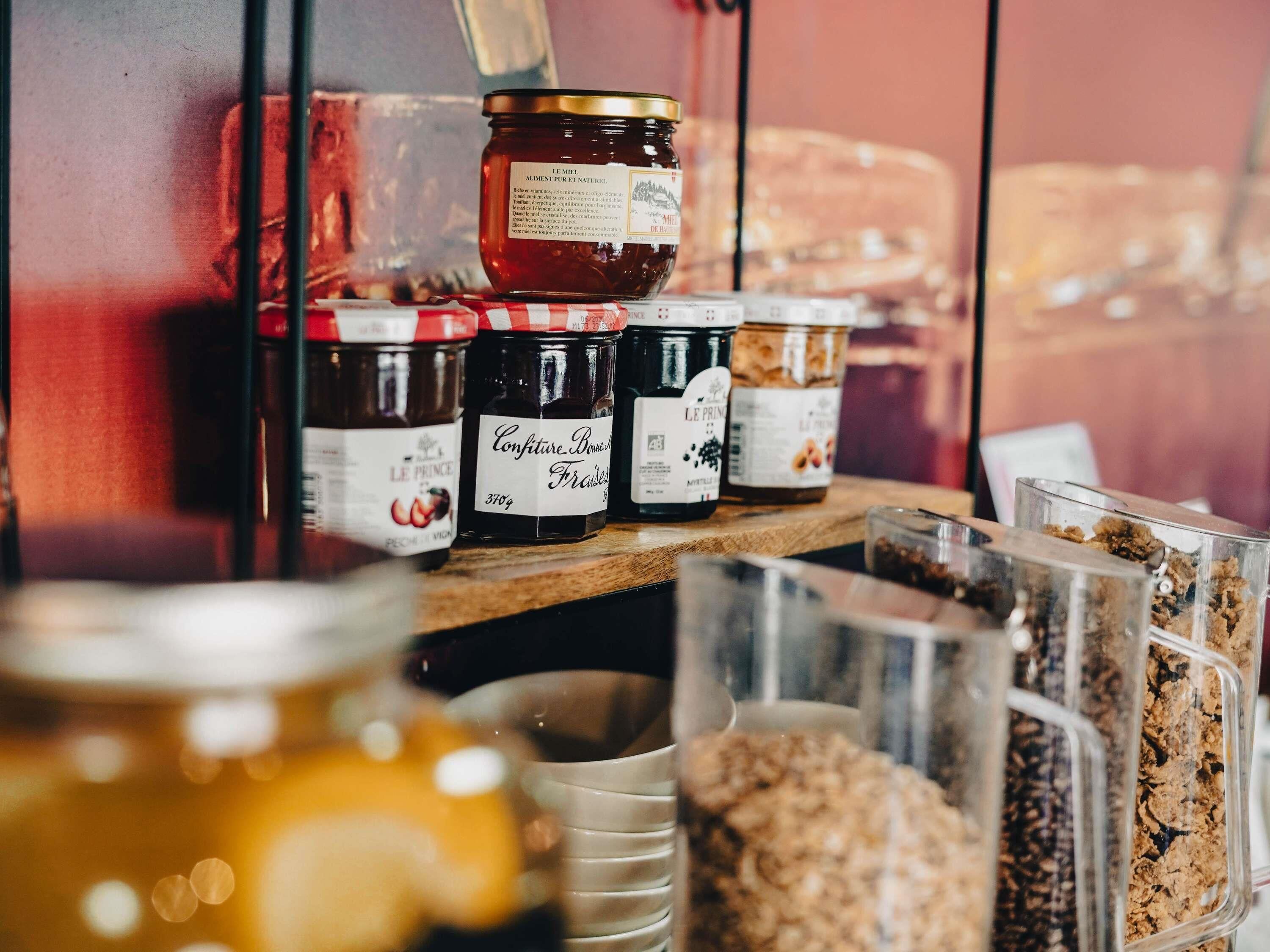 Verschiedene Lebensmittel, darunter Gläser mit Marmelade und Granola, stehen auf einem Regal.