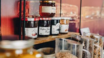 Verschiedene Lebensmittel, darunter Gläser mit Marmelade und Granola, stehen auf einem Regal.