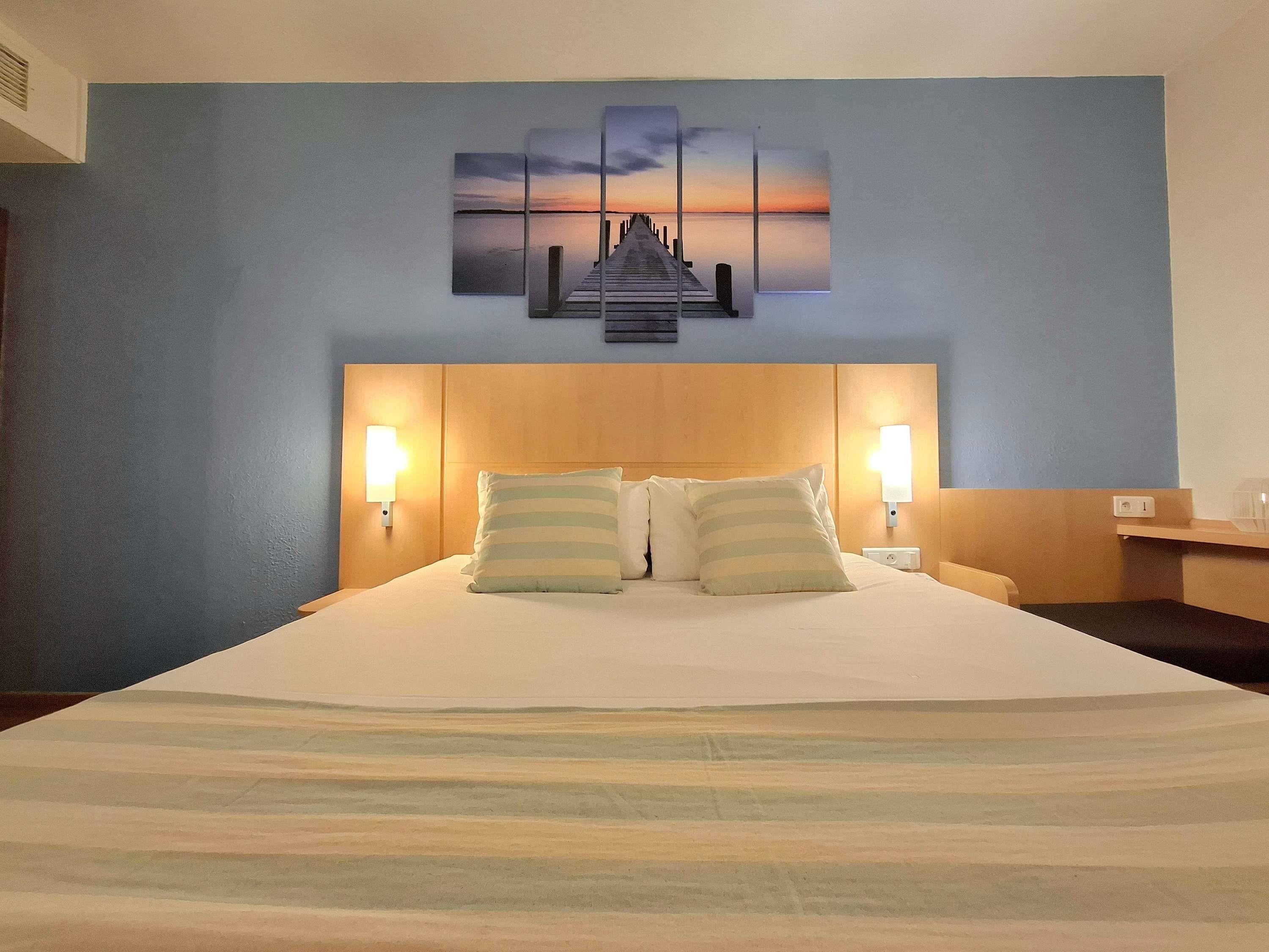 Hotelkamer met een bed, twee bedlampen, een kunstwerk aan de muur en een houten hoofdeinde.