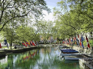 A canal with boats docked, surrounded by trees and flags. - Hôtel ibis Annecy Centre Vieille Ville (Annecy)