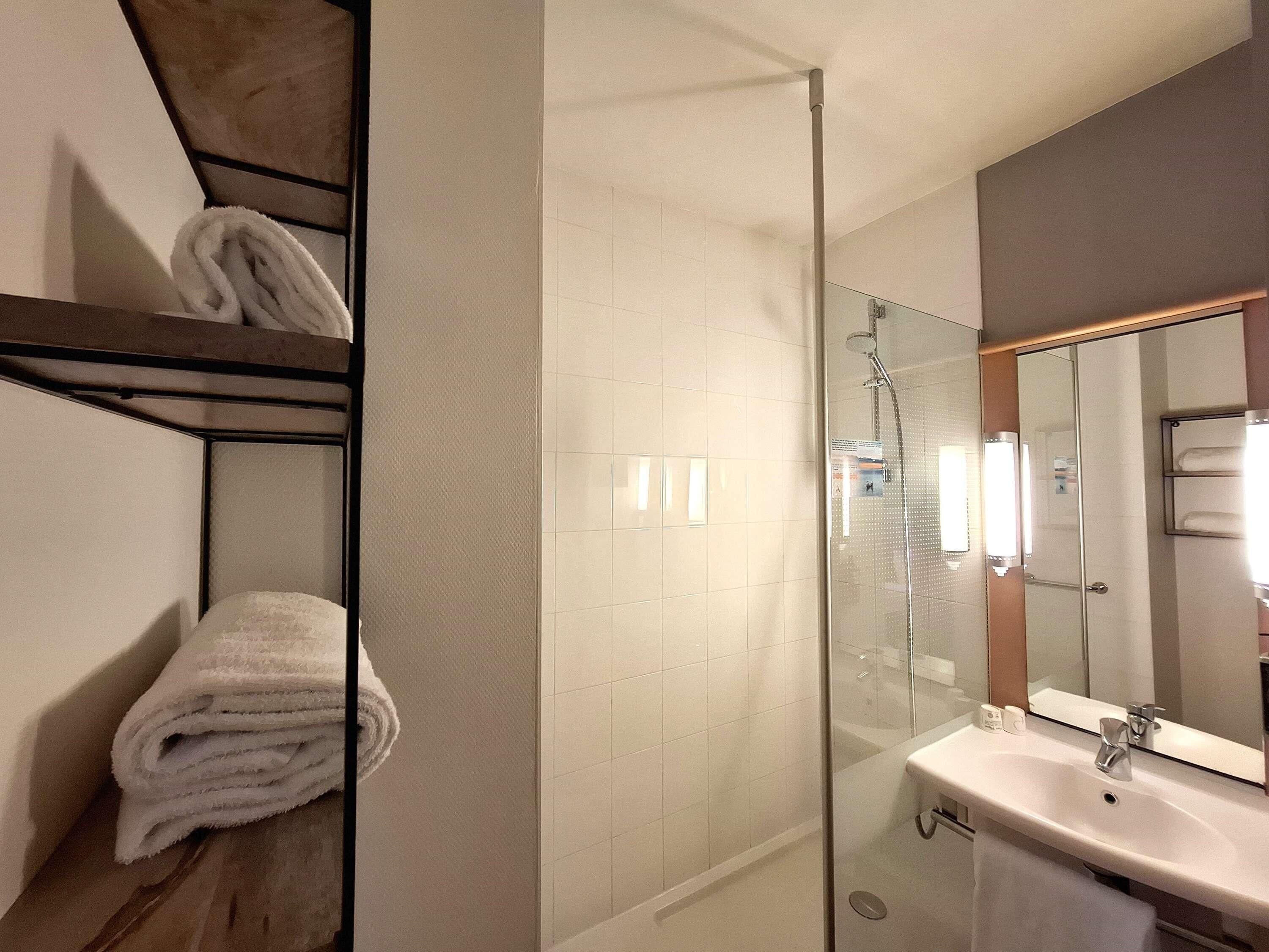 A modern bathroom with a glass shower enclosure, a white sink, and a towel rack with folded towels.