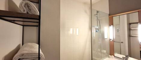 Un baño moderno con cabina de ducha de vidrio, un lavabo blanco y un perchero con toallas dobladas.