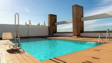 Una piscina con cubierta de madera, barandillas metálicas y una pared blanca con estatuas.