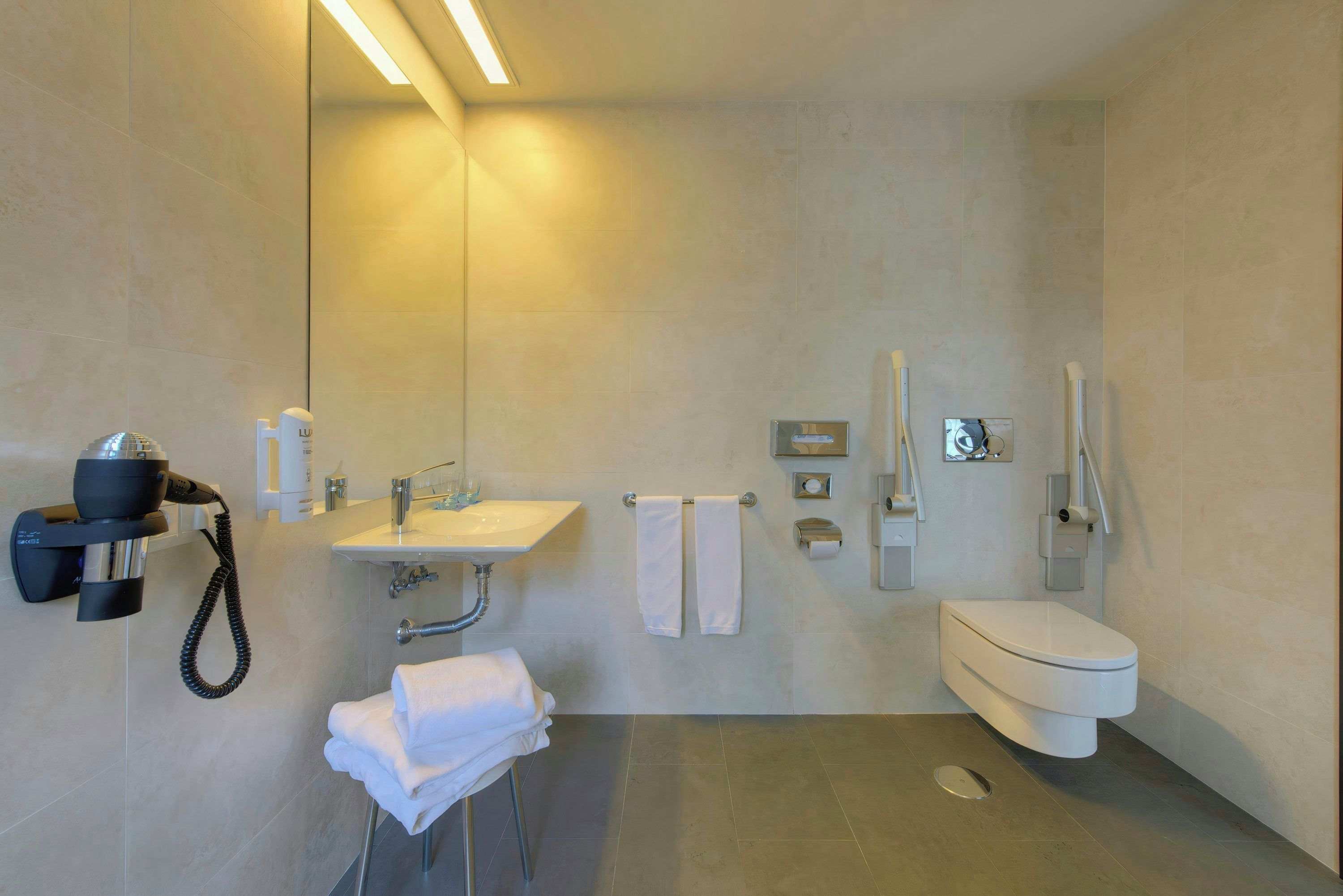 Une salle de bain moderne avec un lavabo intégré, des toilettes, un espace douche et un sèche-cheveux posé sur un support.