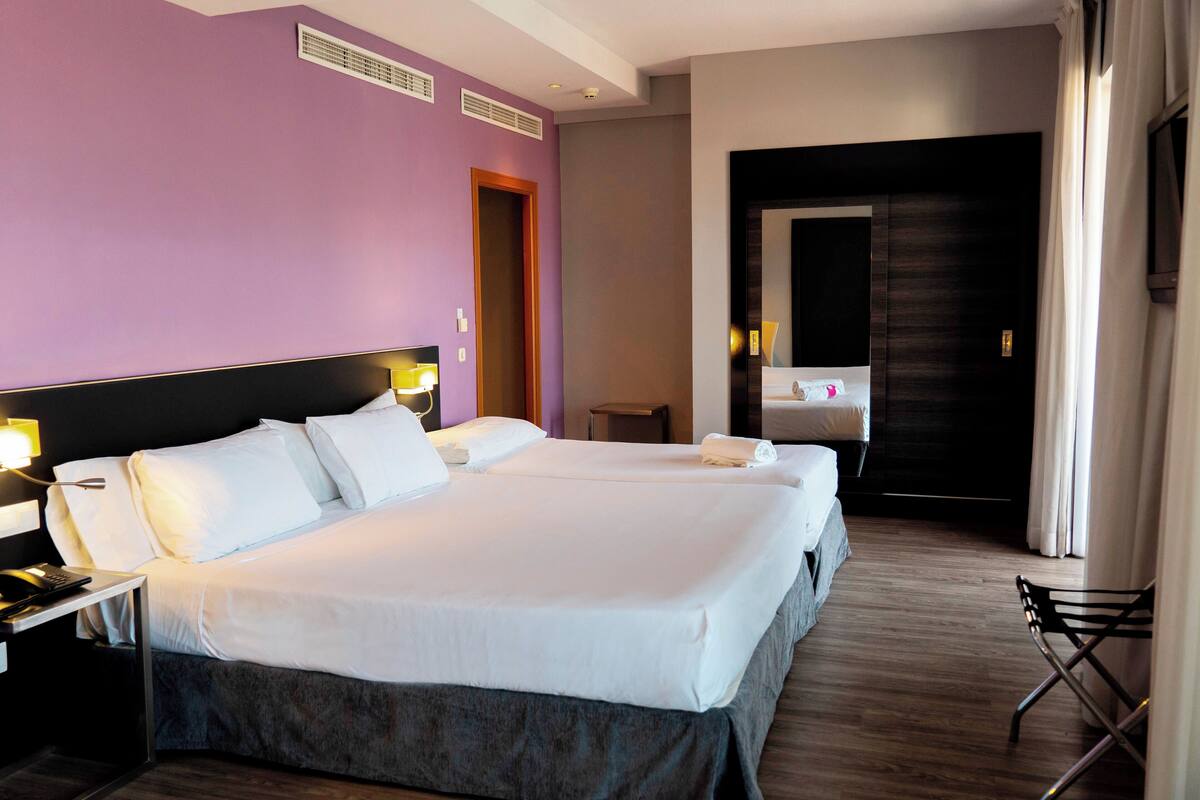 A hotel room with two beds, a desk, and a chair.