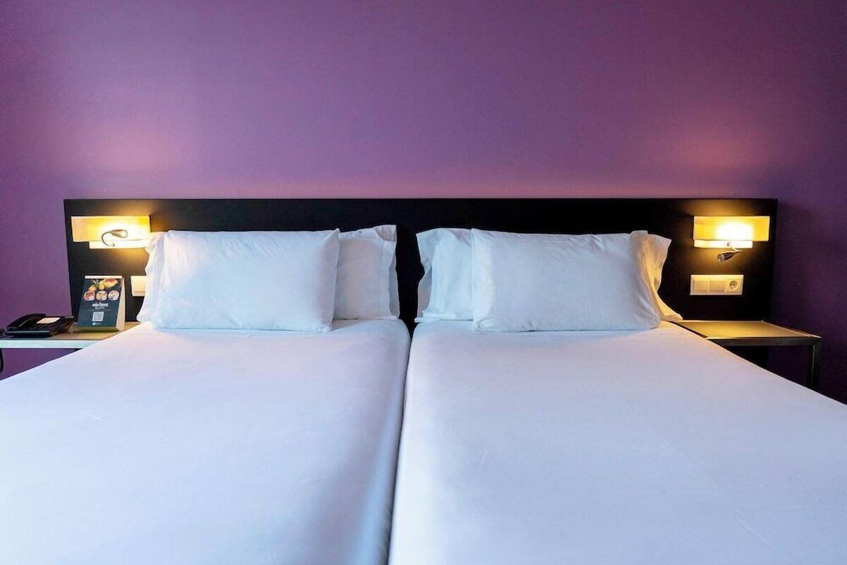 A double bed with white linens, two bedside tables with lamps, and a wall-mounted phone.