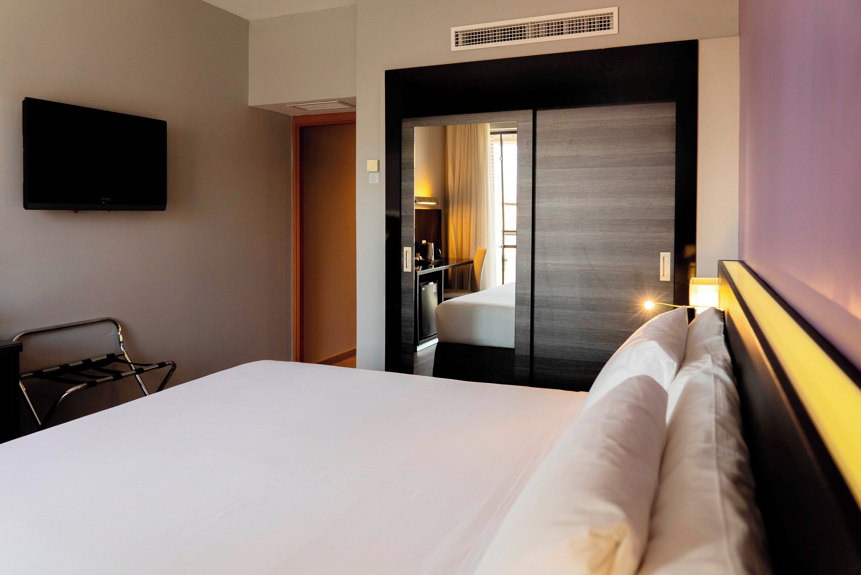 Une chambre d’hôtel avec un lit, un téléviseur fixé au mur, une chaise et un miroir.