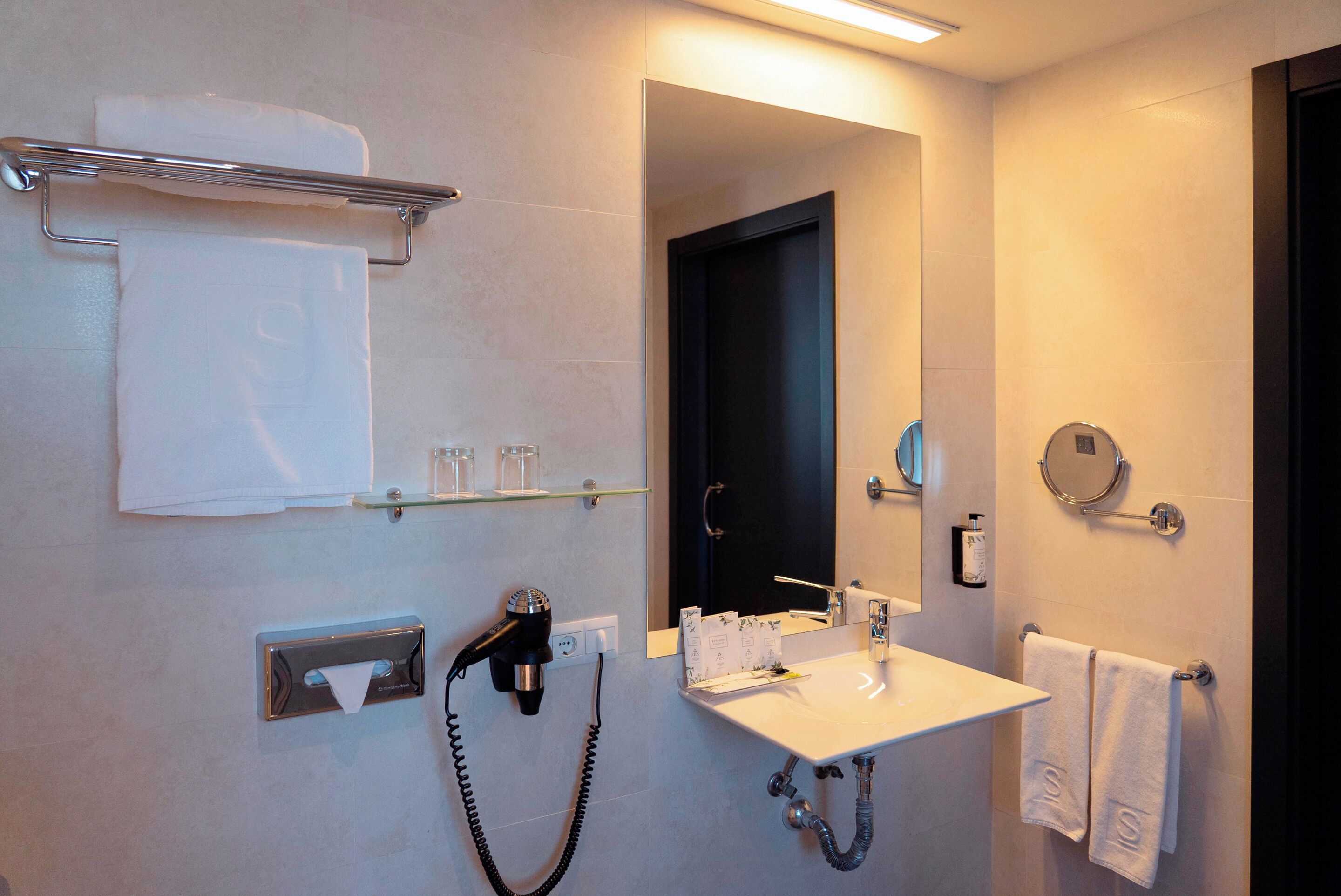 Ein modernes Badezimmer mit Handtuchhalter, Fön, Waschbecken und Spiegel.