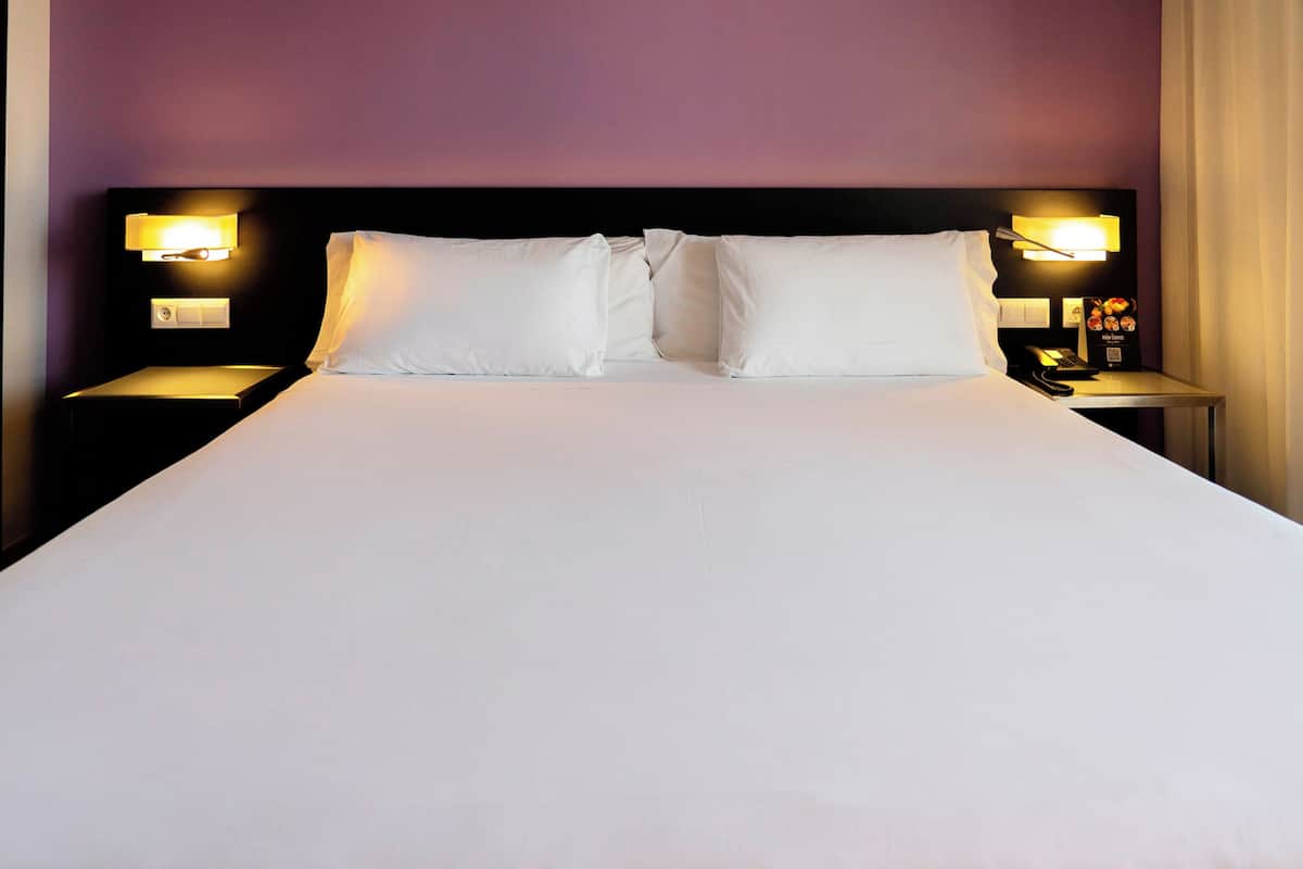 A neatly made bed with white linens and two pillows, flanked by nightstands with lamps and a small clock.