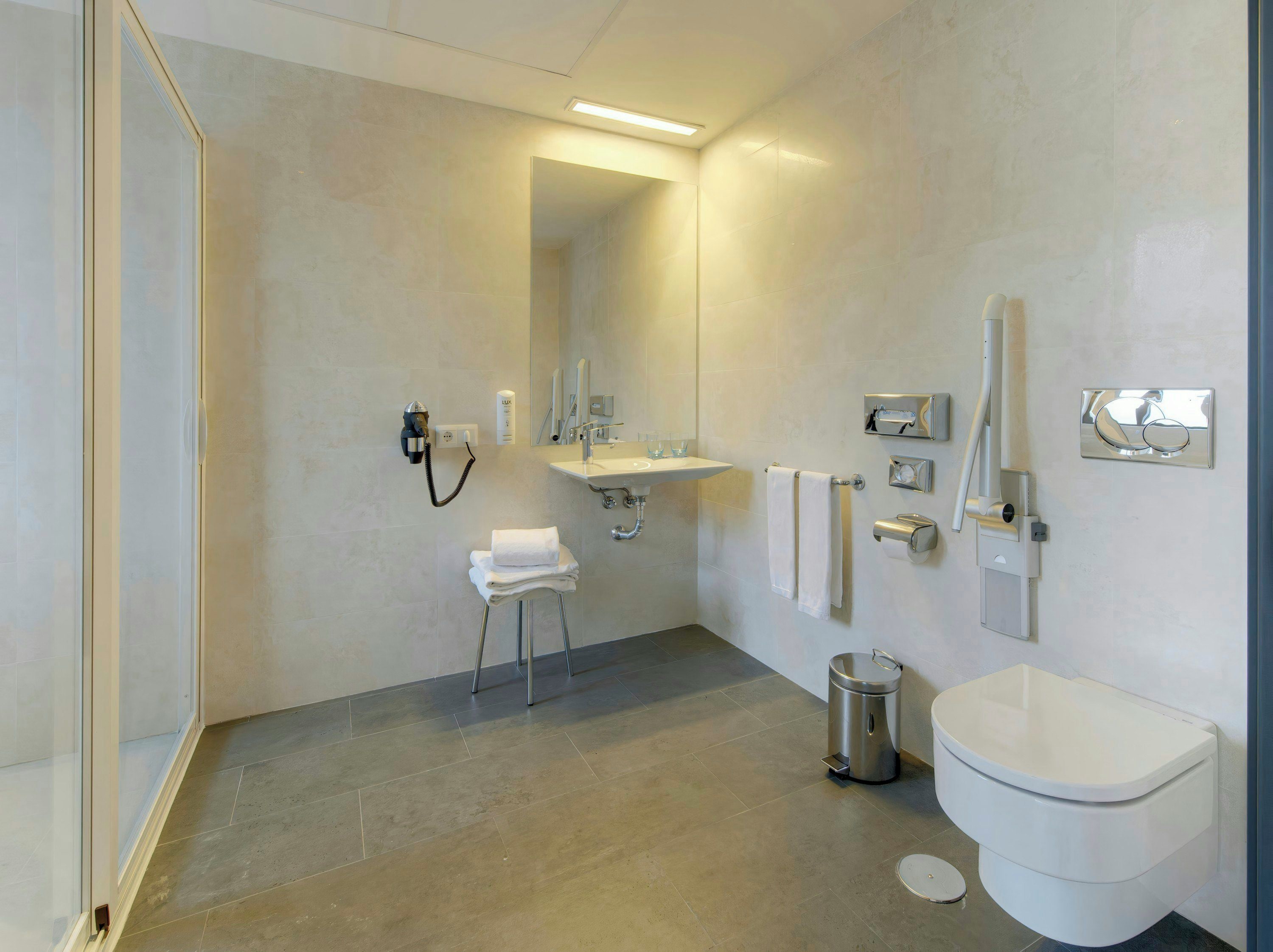 Un baño moderno con lavamanos, espejo, toallero y inodoro.