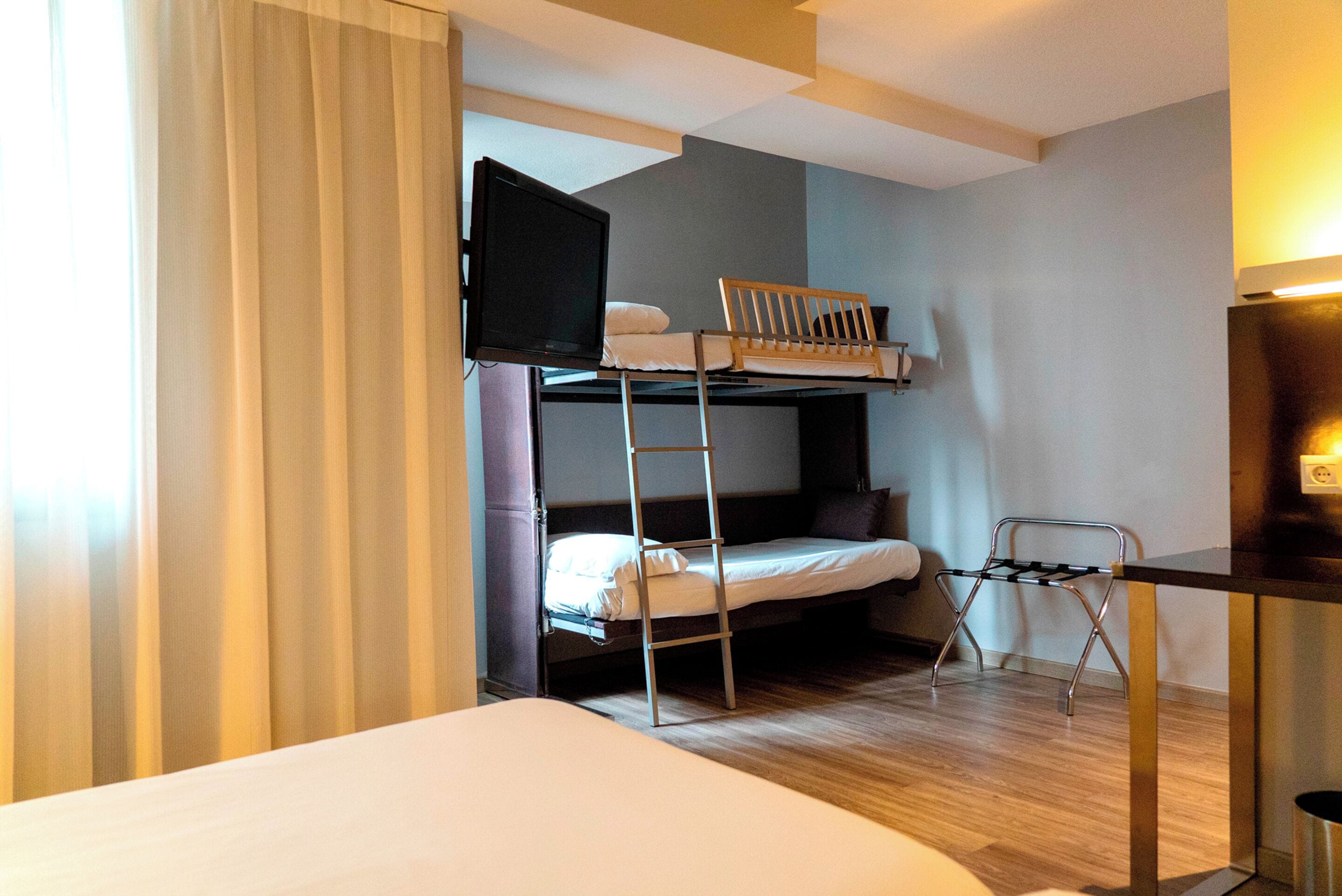 A room with a bunk bed, a desk, a chair, and a television.