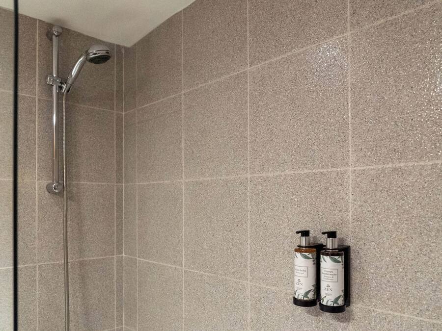 A shower area with a glass door, a handheld showerhead, and two bottles of shampoo and conditioner on the wall.