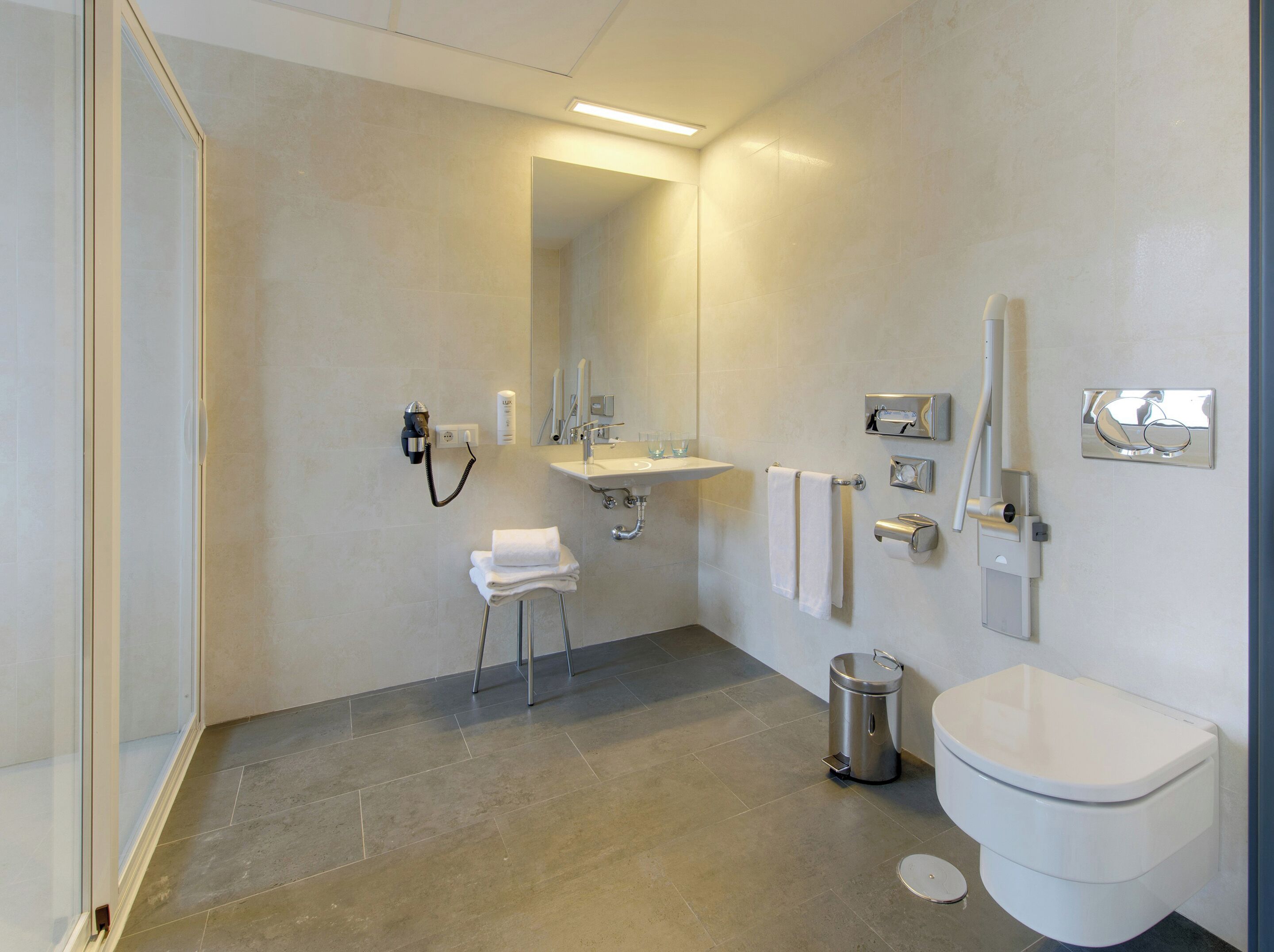 Un baño moderno con ducha, lavamanos, inodoro y un taburete pequeño.