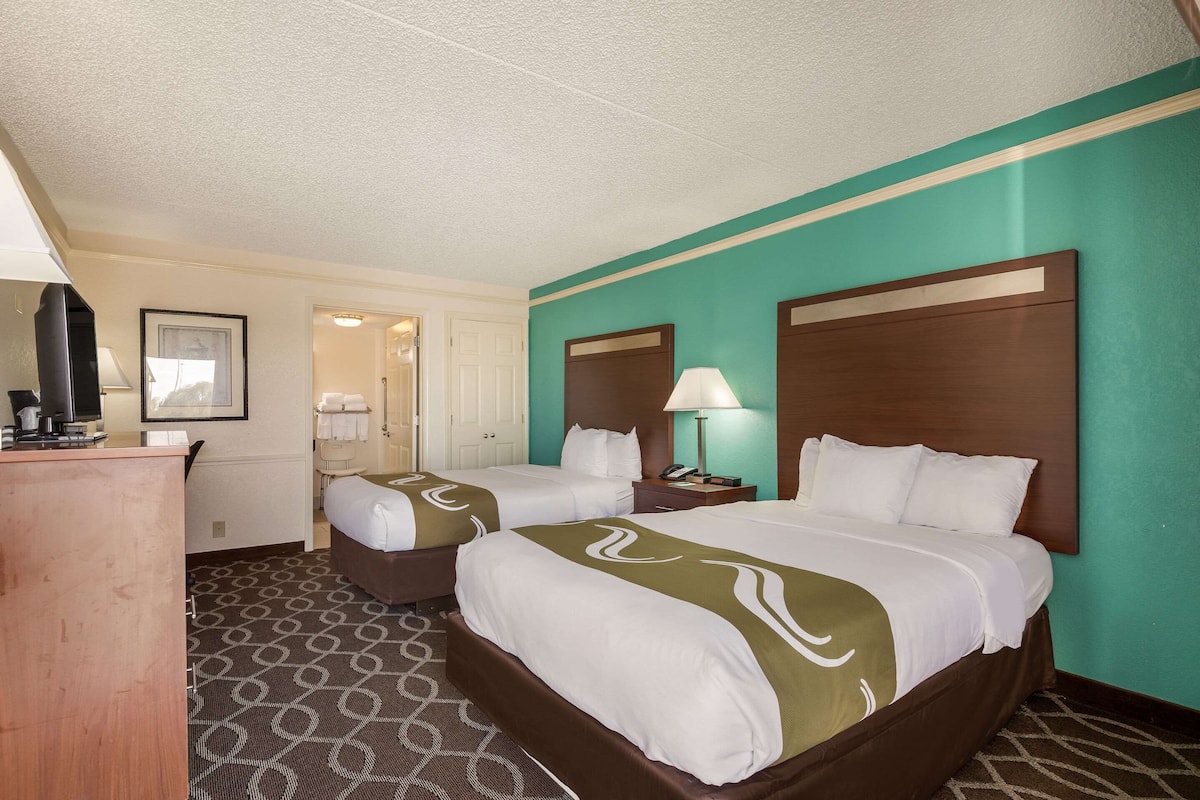 A hotel room with two beds, a desk, a lamp, and a framed picture on the wall.