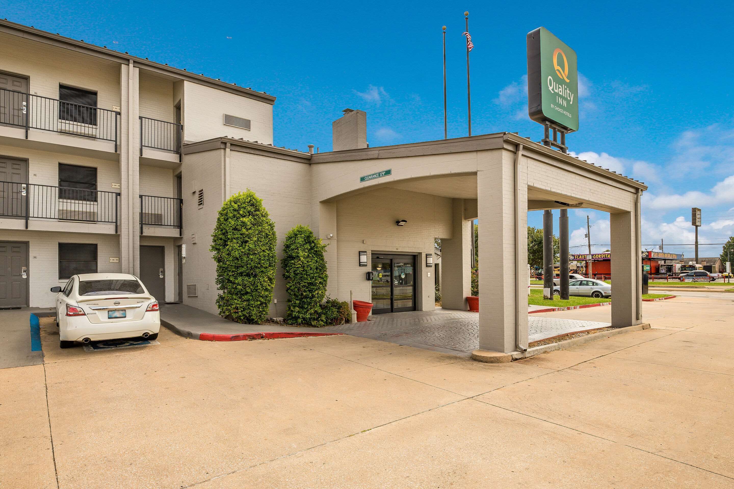 A hotel with a covered entrance, a car parked in front, and a sign indicating it is a Quality Inn.