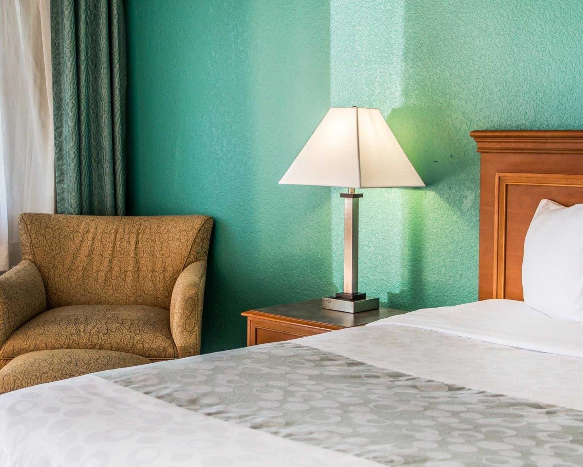 A hotel room with a bed, a nightstand, a lamp, and a chair.