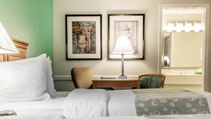 A hotel room with two beds, a desk, a chair, a lamp, and two framed pictures on the wall. - Quality Inn Tulsa Central (Tulsa)