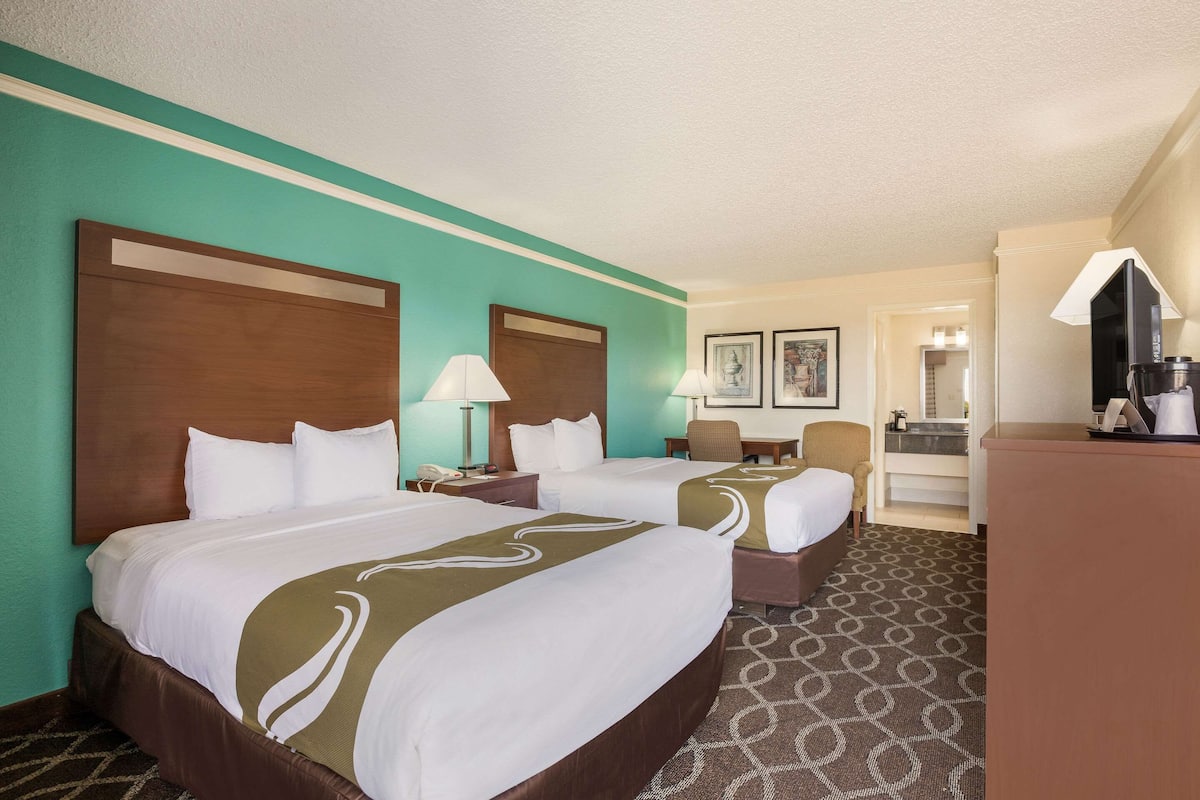 A hotel room with two beds, a desk, a chair, a desk lamp, and a television.