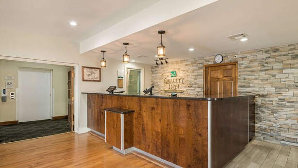 A reception desk with a stone wall backdrop, a clock, and a wooden floor. - Quality Inn Tulsa Central (Tulsa)