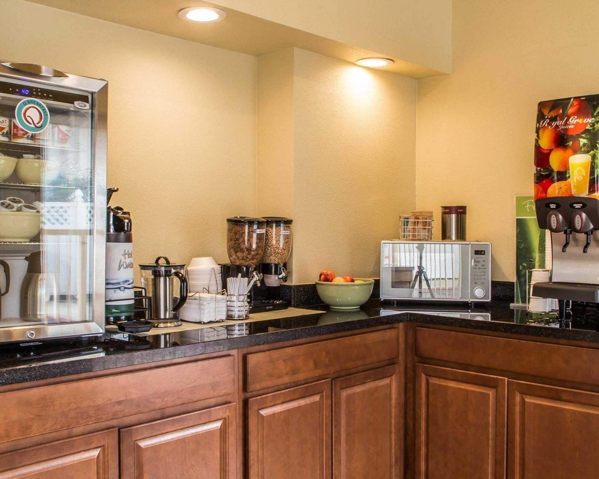Una cocina equipada con cafetera, microondas, dispensador de fruta y estación de café.