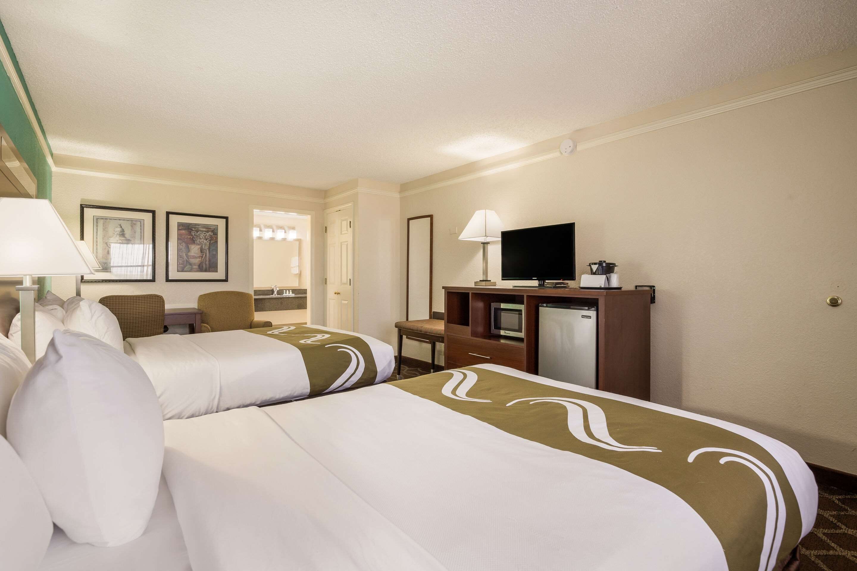 A hotel room with two beds, a desk, a television, and a minibar.