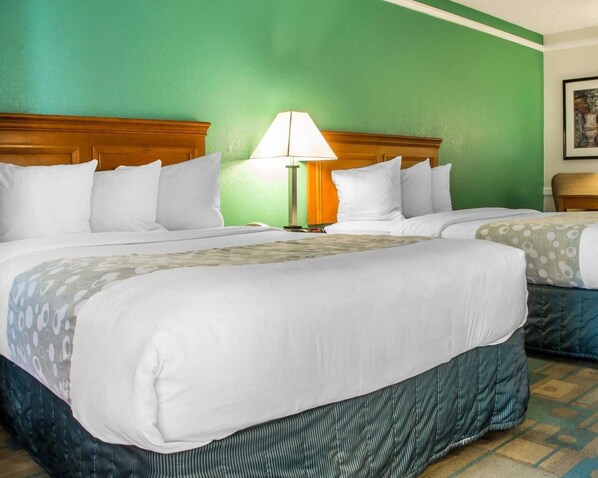 A hotel room with two beds, a nightstand with a lamp, and a green wall.