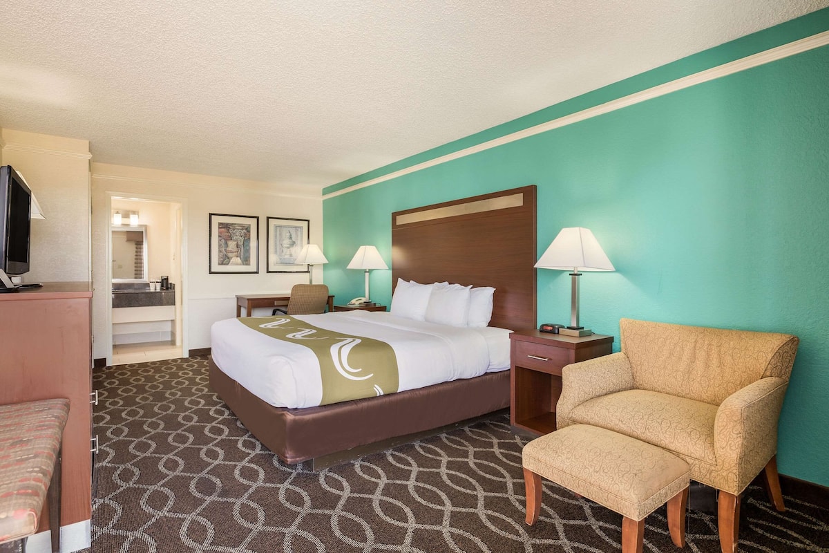 A hotel room with a bed, a chair, a desk, a television, and a bathroom.