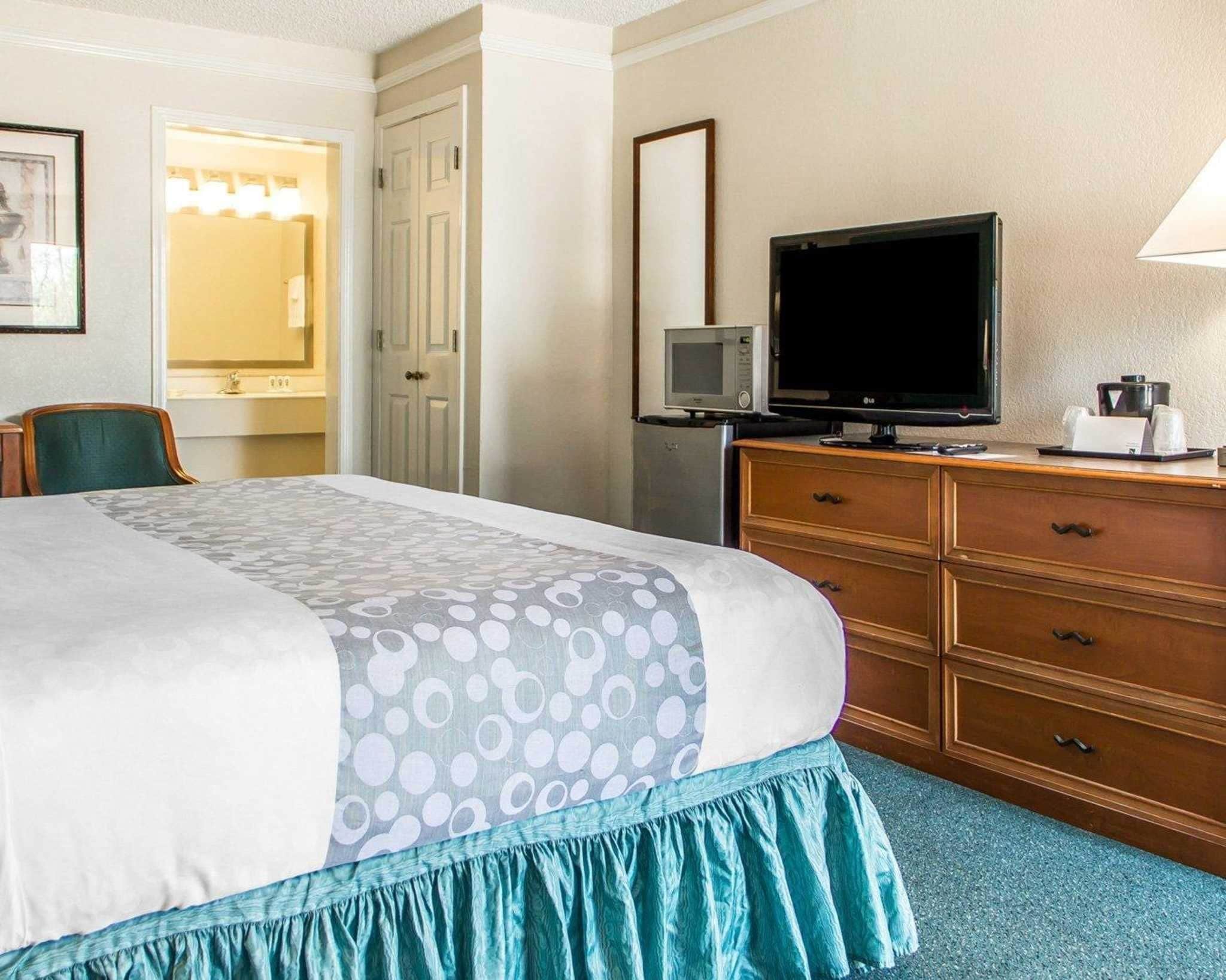 A hotel room with a large bed, a television, a dresser, and a mirror.