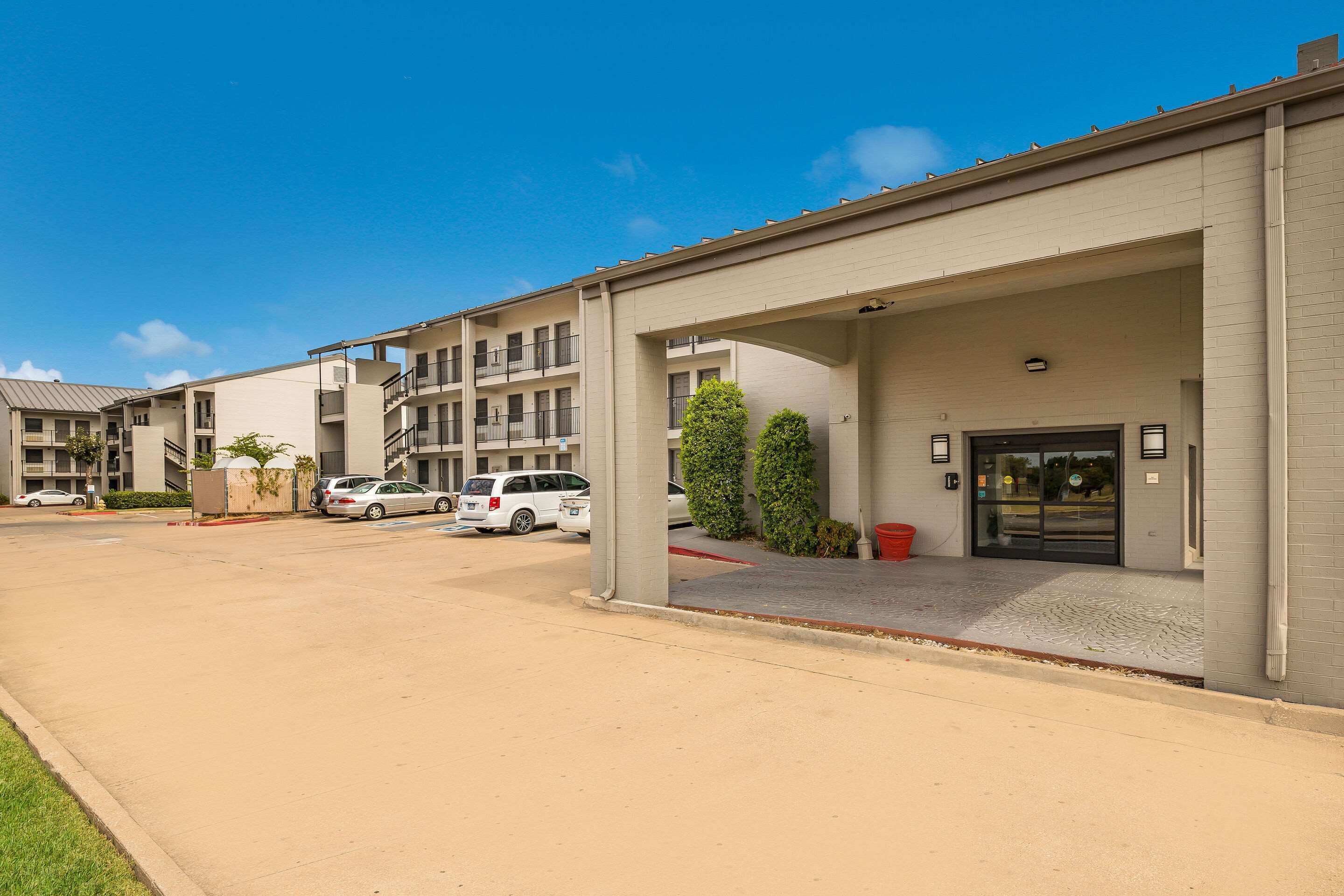 A modern building with a covered entrance, multiple balconies, and a parking area with cars.